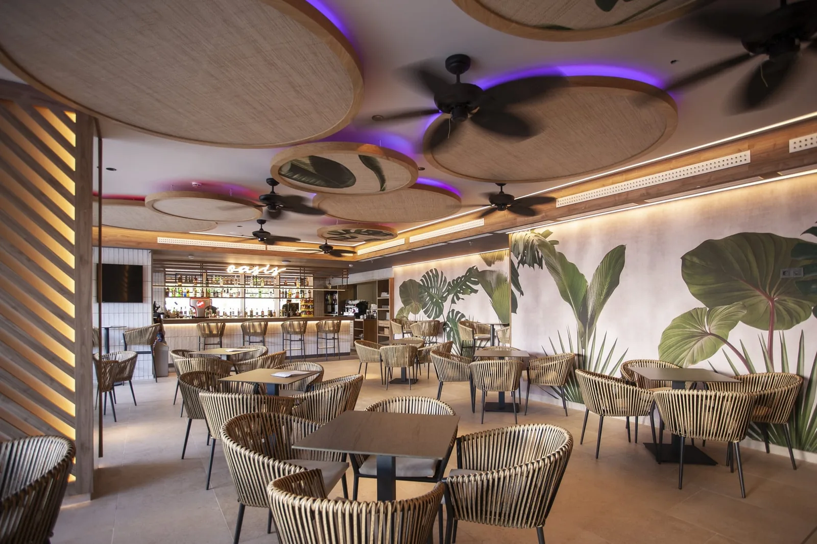 Comedor tropical del restaurante Exótico con mural de hojas y sillas de mimbre